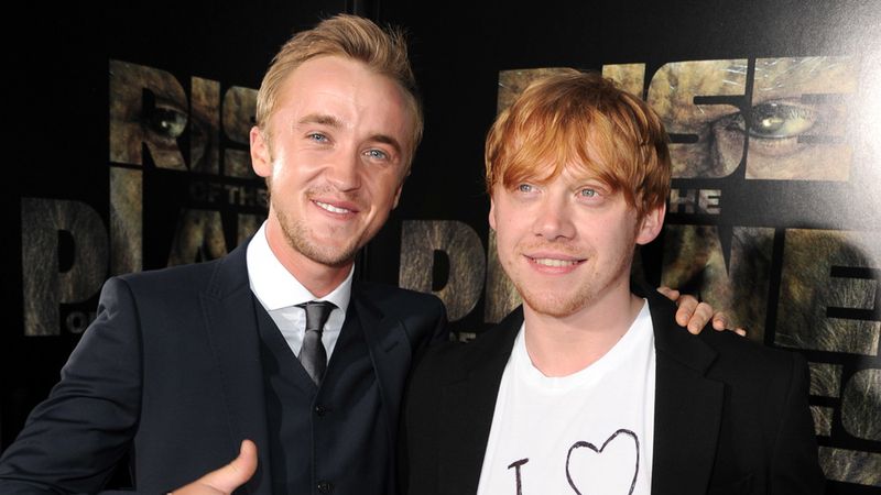 Tom Felton e Rupert Grint sorrindo enquanto posavam de braços dados na estreia de um filme