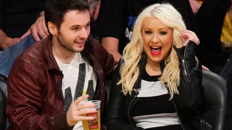 Matthew Rutler e Christina Aguilera sentados na quadra em um jogo do Lakers em 2012