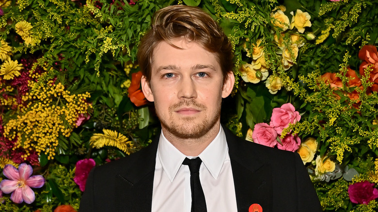   Joe Alwyn posant davant d'una paret de flors