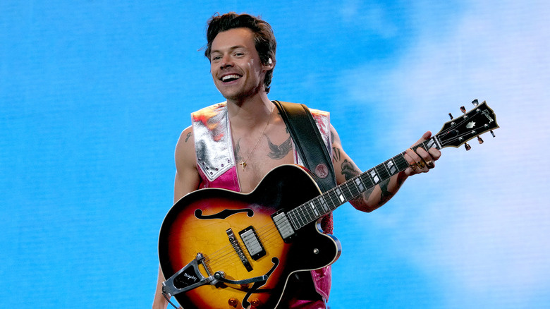   Harry Styles a l'escenari sostenint una guitarra i somrient