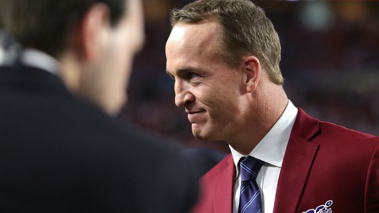 Peyton Manning sorrindo de blazer vermelho
